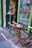 A creatively designed bicycle with an unusual metallic and mechanical structure is parked outside a shop. A skeleton is posed at a table next to the shop's entrance, which is highlighted with green paint. The window displays various bottles of absinthe and advertises the store as an absinthe bar.