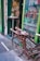 A creatively designed bicycle with an unusual metallic and mechanical structure is parked outside a shop. A skeleton is posed at a table next to the shop's entrance, which is highlighted with green paint. The window displays various bottles of absinthe and advertises the store as an absinthe bar.