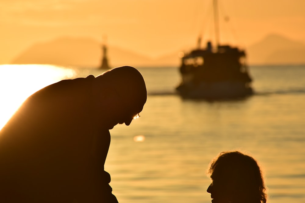 silhueta do homem em pé perto do corpo de água durante o pôr do sol