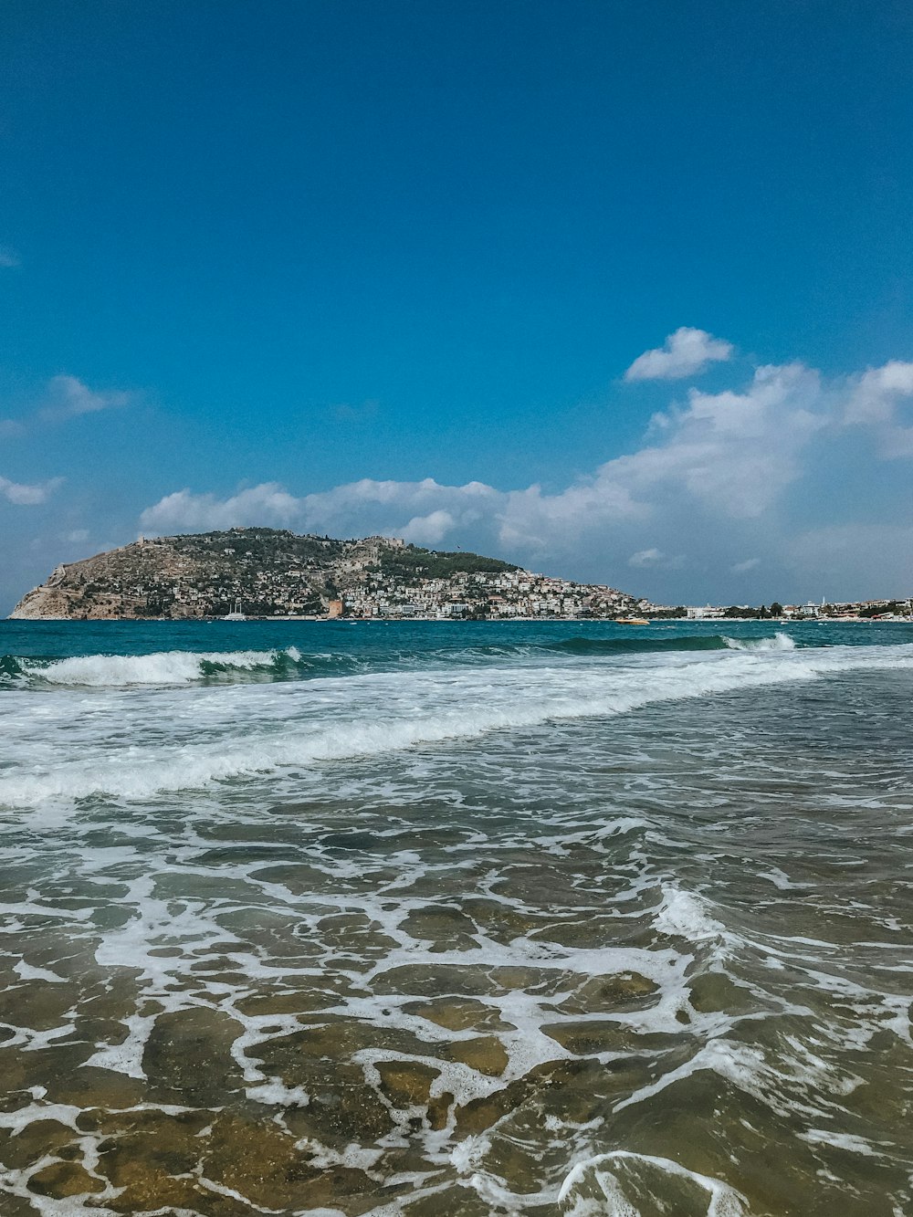 昼間の青空の下で海に浮かぶ茶色と緑の岩層