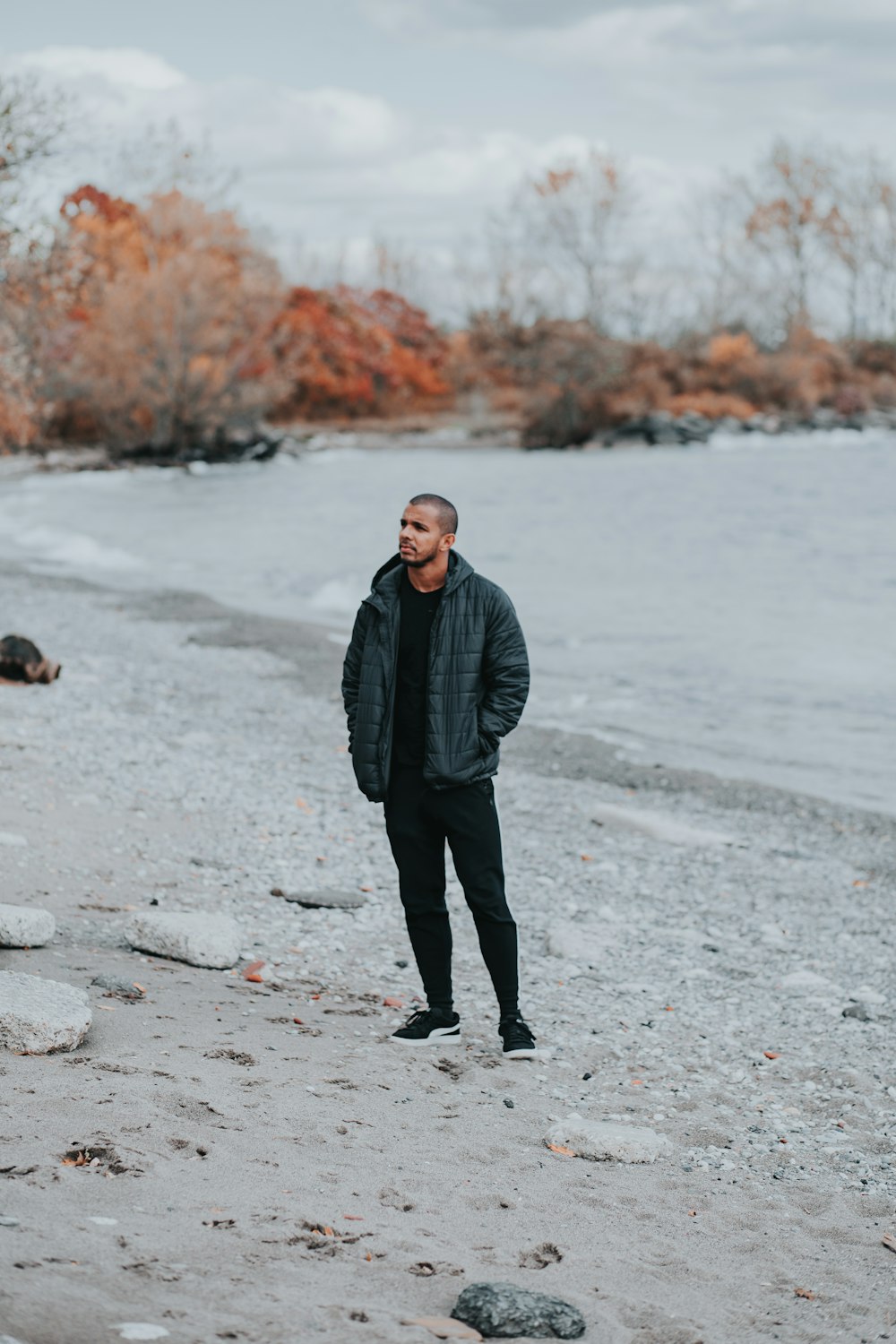 man in black jacket standing on gray sand during daytime