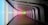 A modern, curving hallway with a futuristic design features illuminated walls displaying a gradient of colors ranging from blue to pink to green. The space has a sleek and minimalistic appearance with dark accents and a wooden floor.