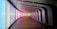 A modern, curving hallway with a futuristic design features illuminated walls displaying a gradient of colors ranging from blue to pink to green. The space has a sleek and minimalistic appearance with dark accents and a wooden floor.