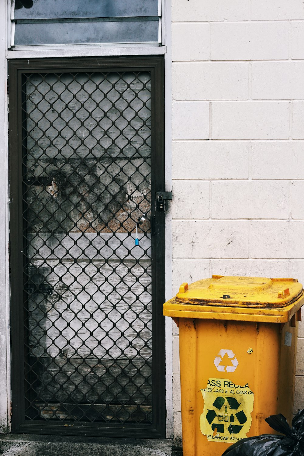 yellow trash bin beside gray concrete wall