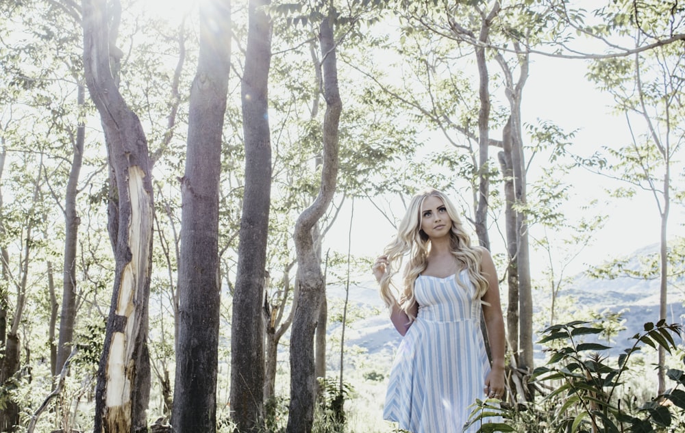 woman in white and blue striped dress standing under trees during daytime