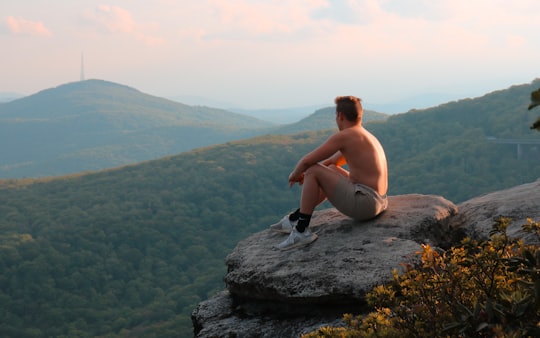 man in black shorts sitting on rock formation during daytime in Blue Ridge Mountains United States