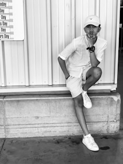 man in white t-shirt and white shorts sitting on white wooden wall