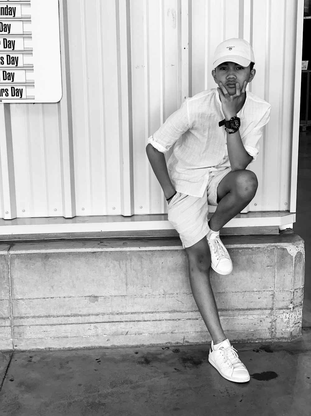 homme en t-shirt blanc et short blanc assis sur un mur en bois blanc