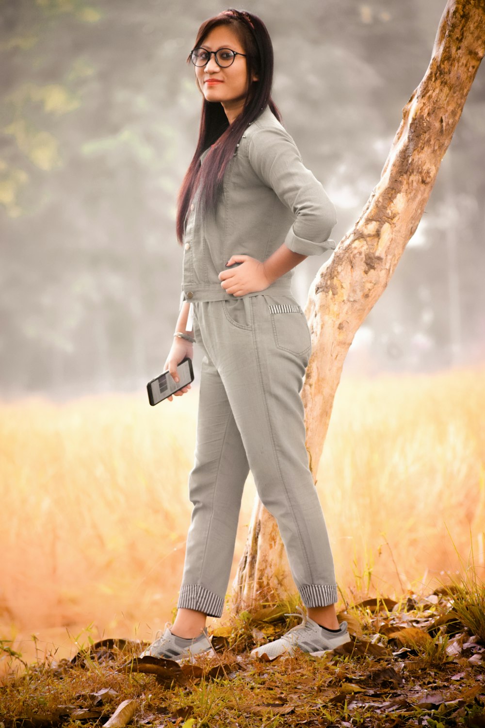 woman in gray jacket and brown pants standing on brown tree trunk during daytime