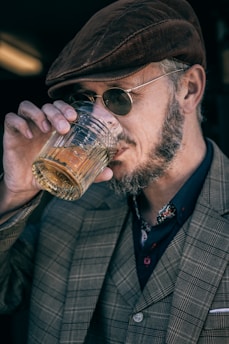 man in black and white plaid suit jacket holding clear drinking glass