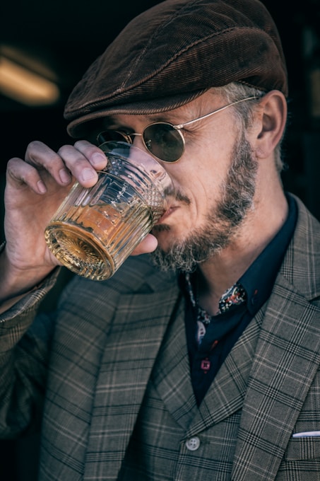 man in black and white plaid suit jacket holding clear drinking glass
