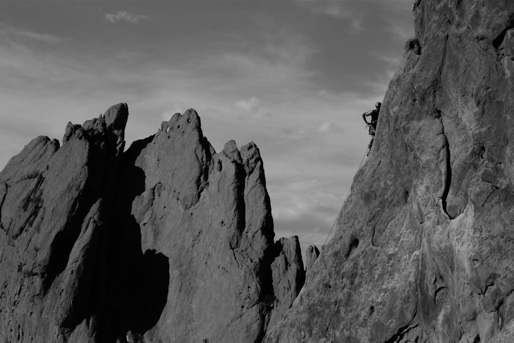 grayscale photo of person climbing on rock formation