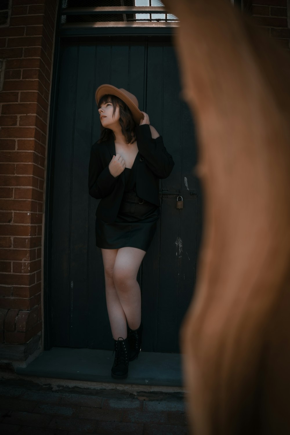 woman in black long sleeve shirt and black stockings leaning on brown brick wall