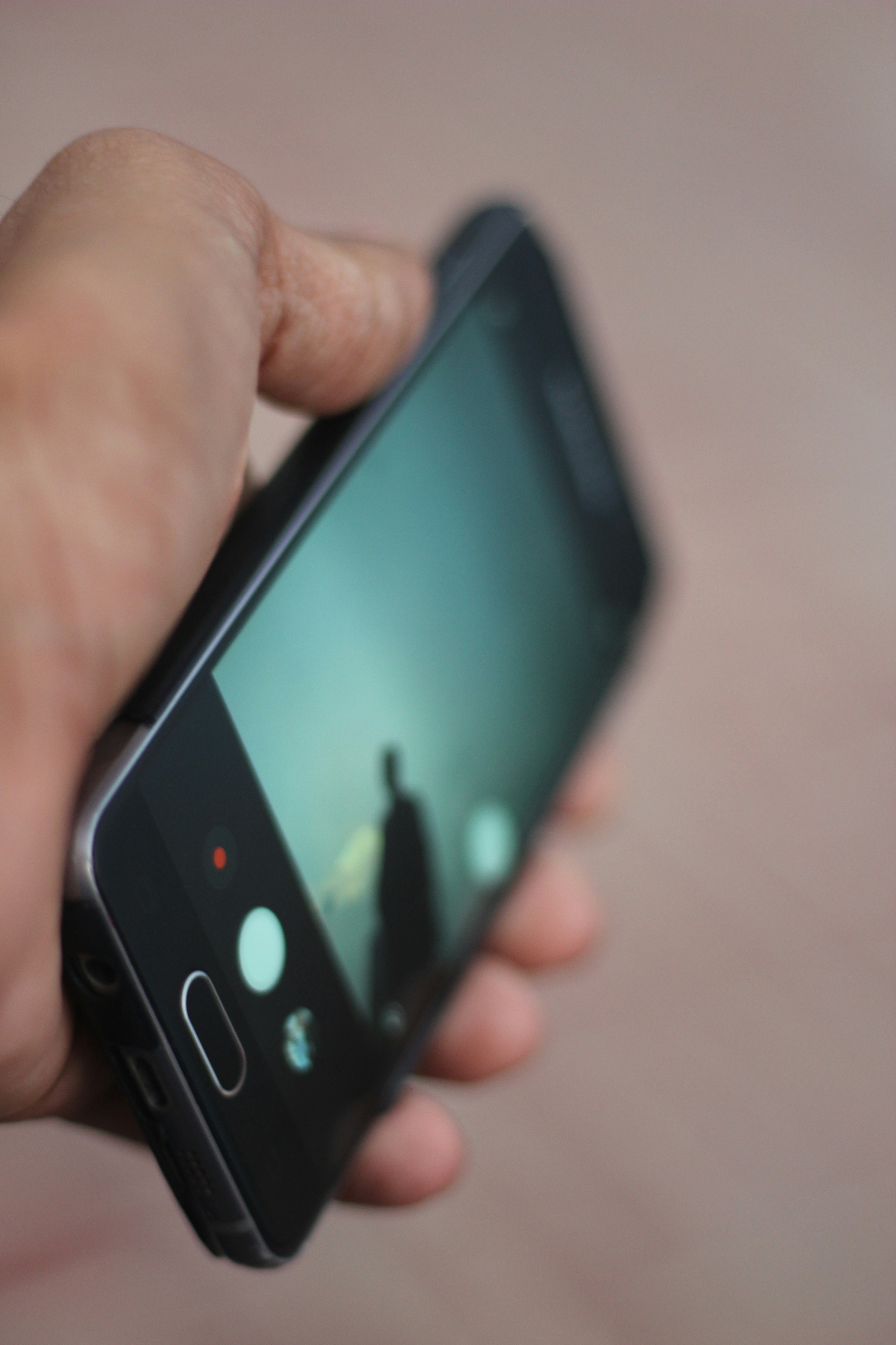 Flagship smartphone held in hand, dark background, screen illuminating face, dramatic lighting