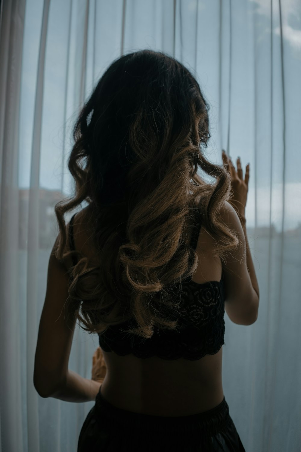Mujer en sostén de encaje negro y braga de pie cerca de la ventana