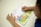 A child is reading a picture book with colorful illustrations of animals and a farmer in a natural setting. The child's hands are visible, holding the book open on a white surface.