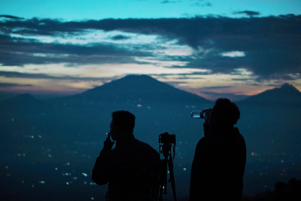 silhouette of 2 men standing near mountain during sunset