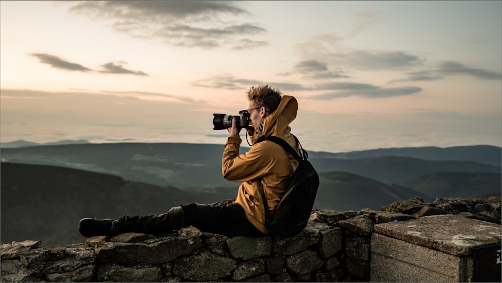 uomo in giacca marrone che scatta foto di montagna durante il giorno