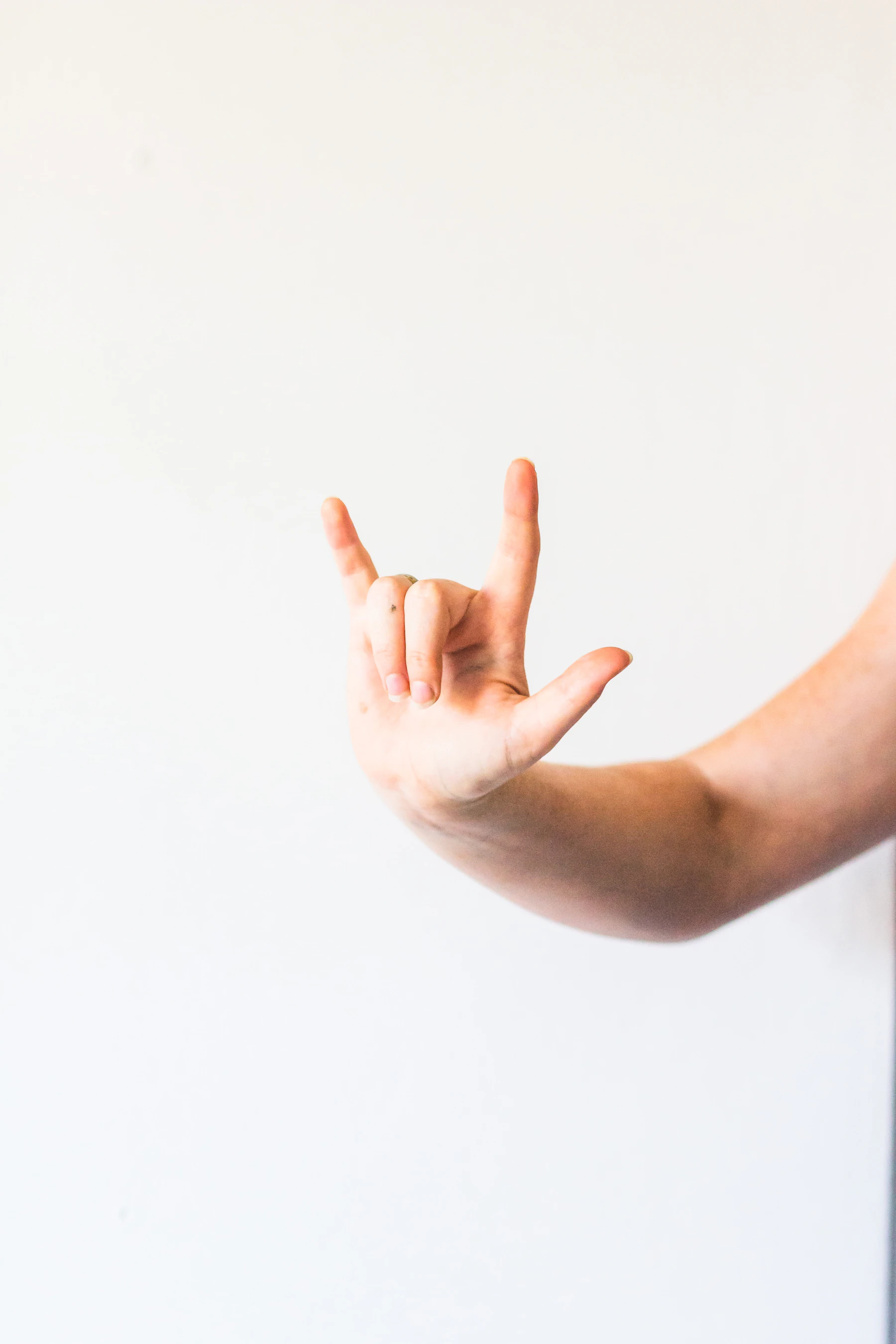 A hand held up against a white wall with the thumb, index finger and little finger extended