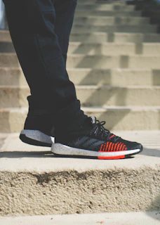 Close-up of black and white sneakers with orange accents resting on graffiti-covered steps.