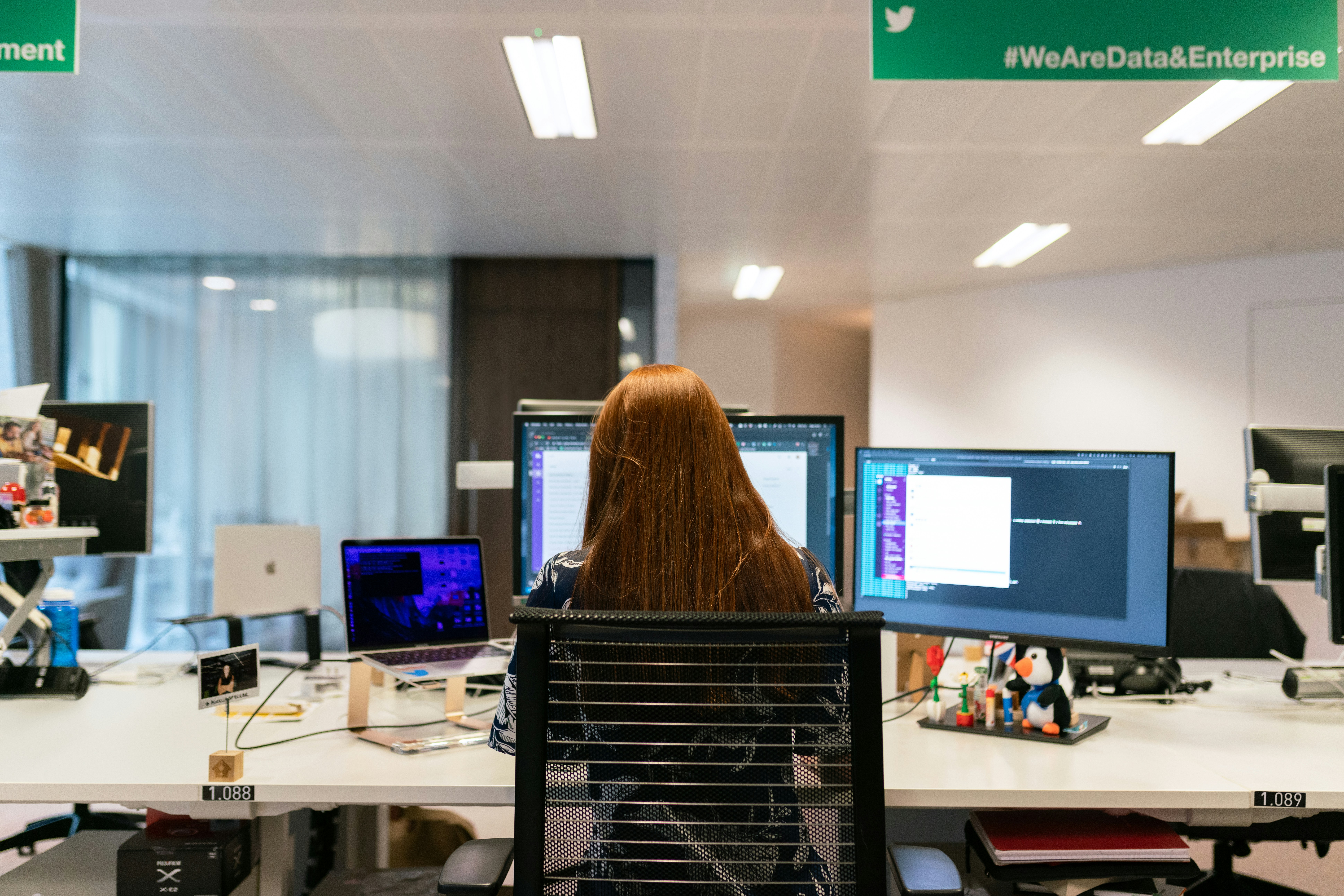 Female software engineer works at desk with computers, coding