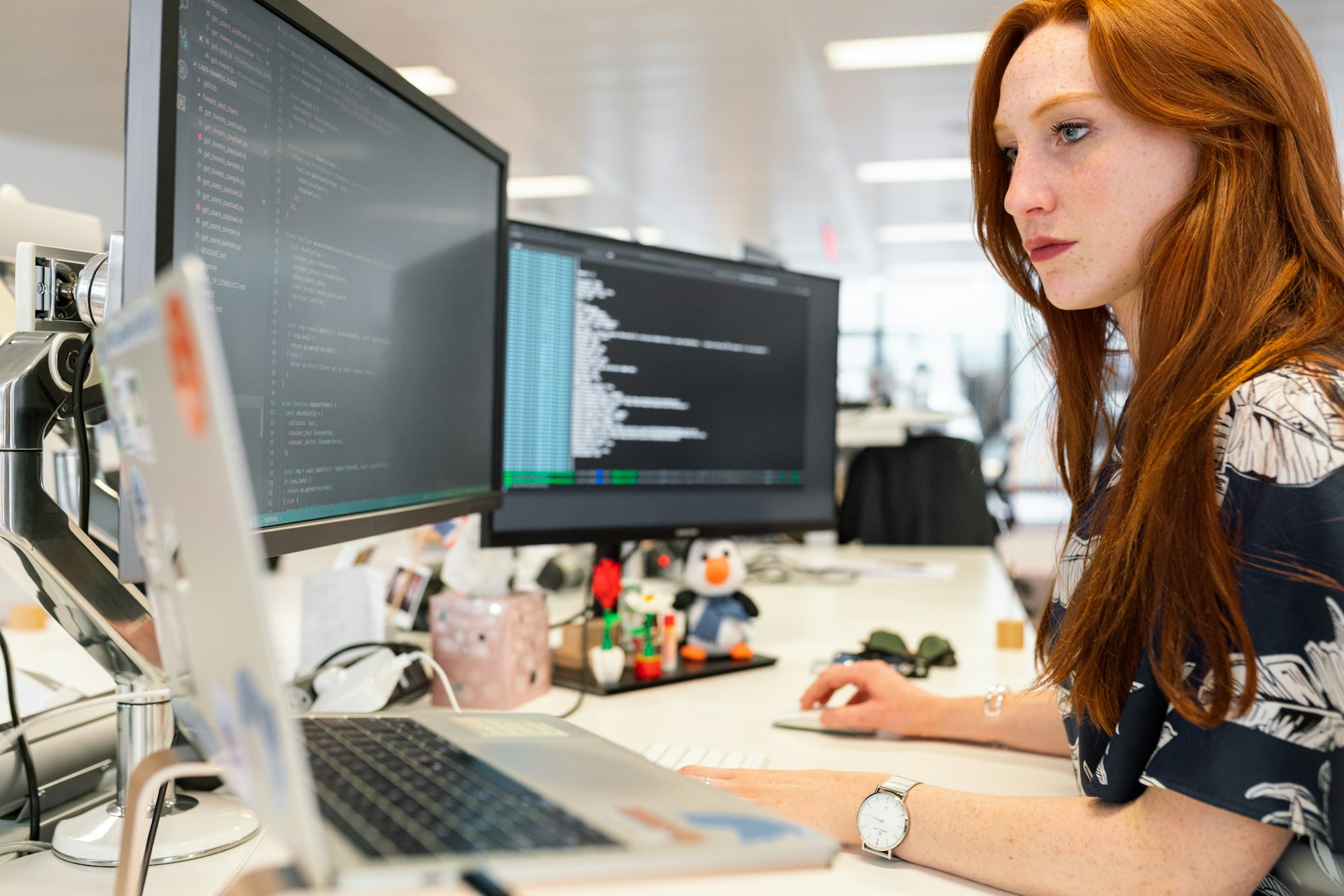 A software engineer, right, looking at a 3-monitor setup while working.