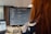 A person is sitting at a desk, focusing on a computer screen displaying code. The individual appears to be programming or debugging. The setup includes a large monitor and a laptop, surrounded by muted office lighting.