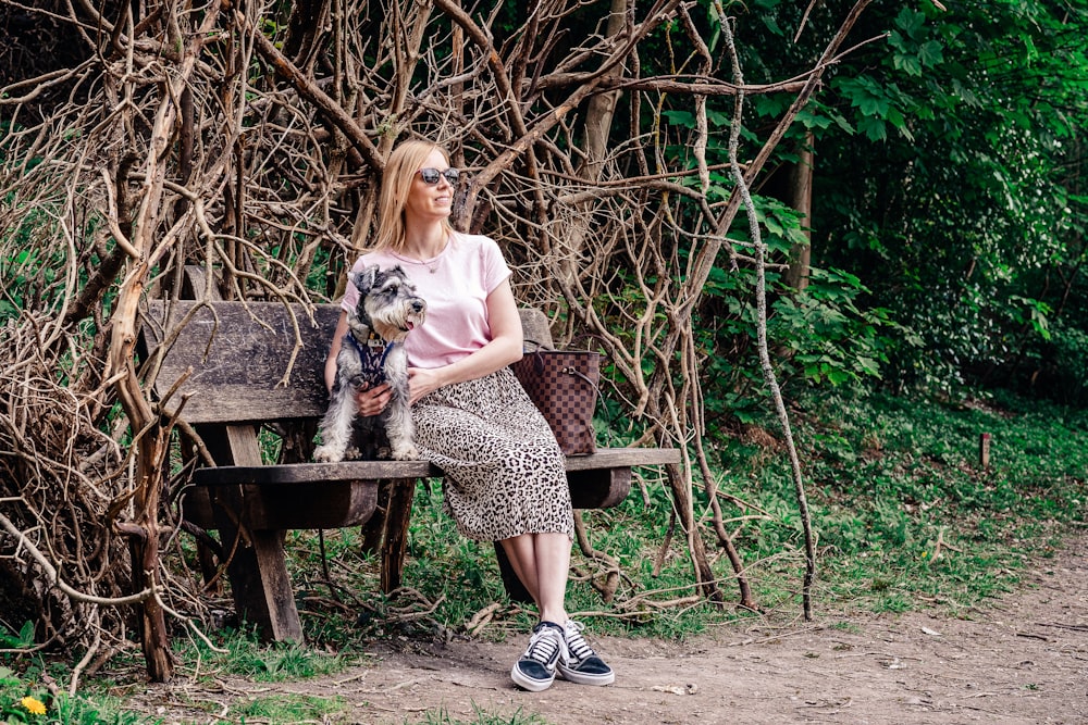 woman in pink shirt sitting on brown wooden bench with black and white long coated small