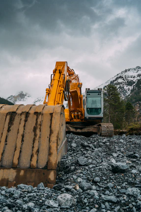 Massive yellow excavator working at a rocky mining site under a bright sky.