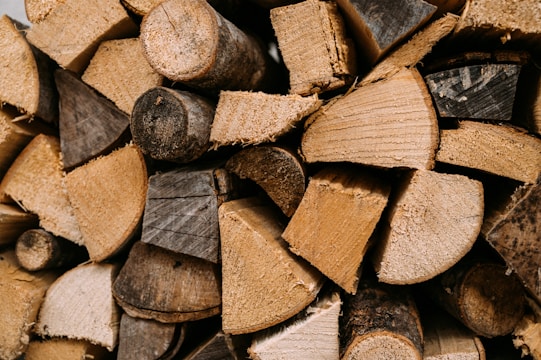 A close-up view of neatly stacked firewood, showcasing different shades and textures of wood with visible growth rings and rough-cut surfaces.
