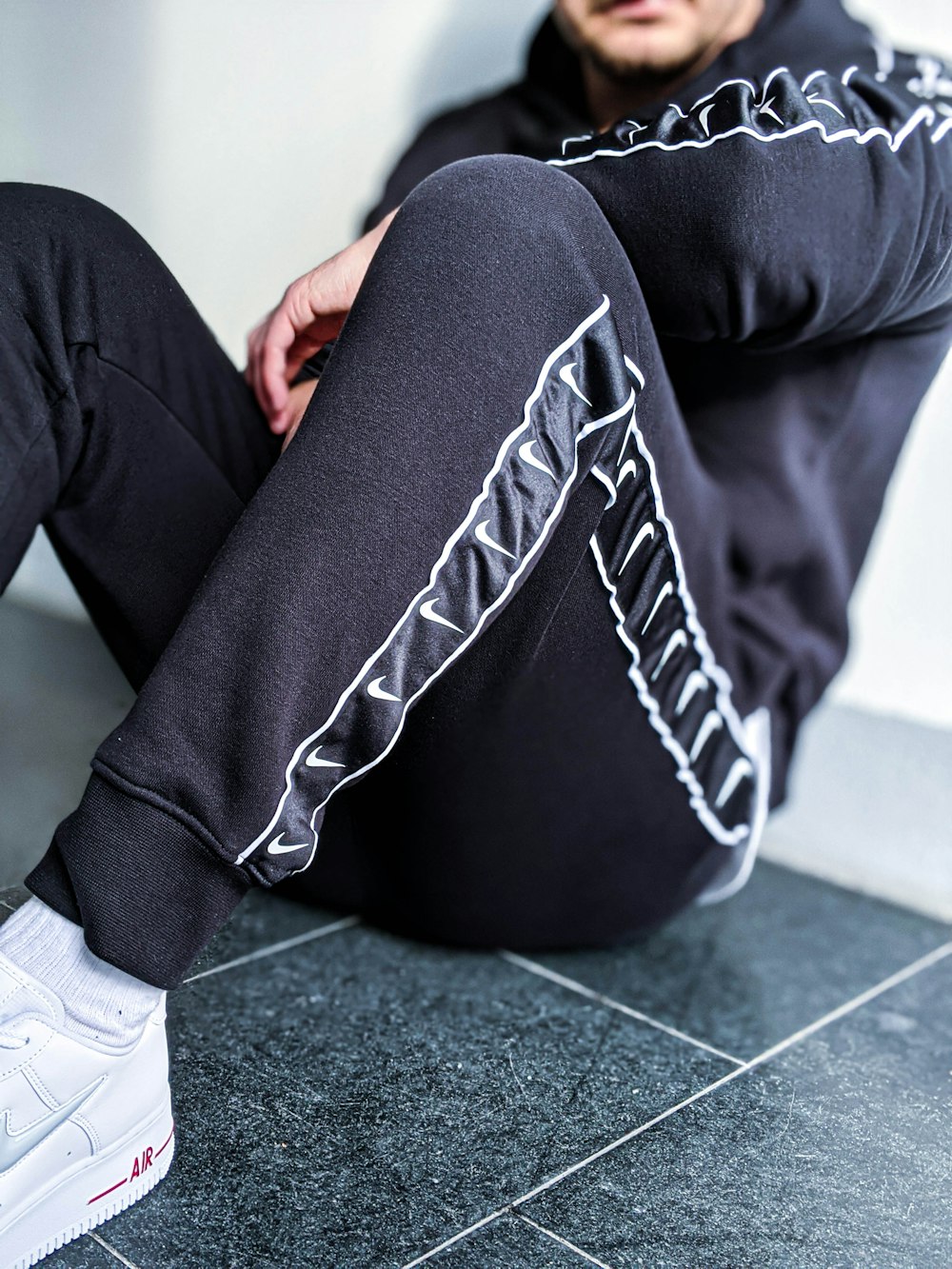 person in black and white pants and white sneakers sitting on gray floor tiles