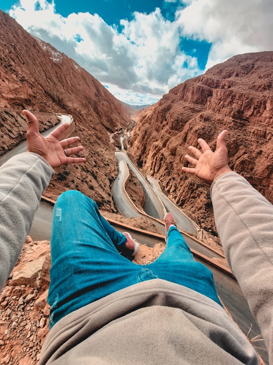 person in gray pants sitting on brown rock formation during daytime in Boumalne Dades Morocco