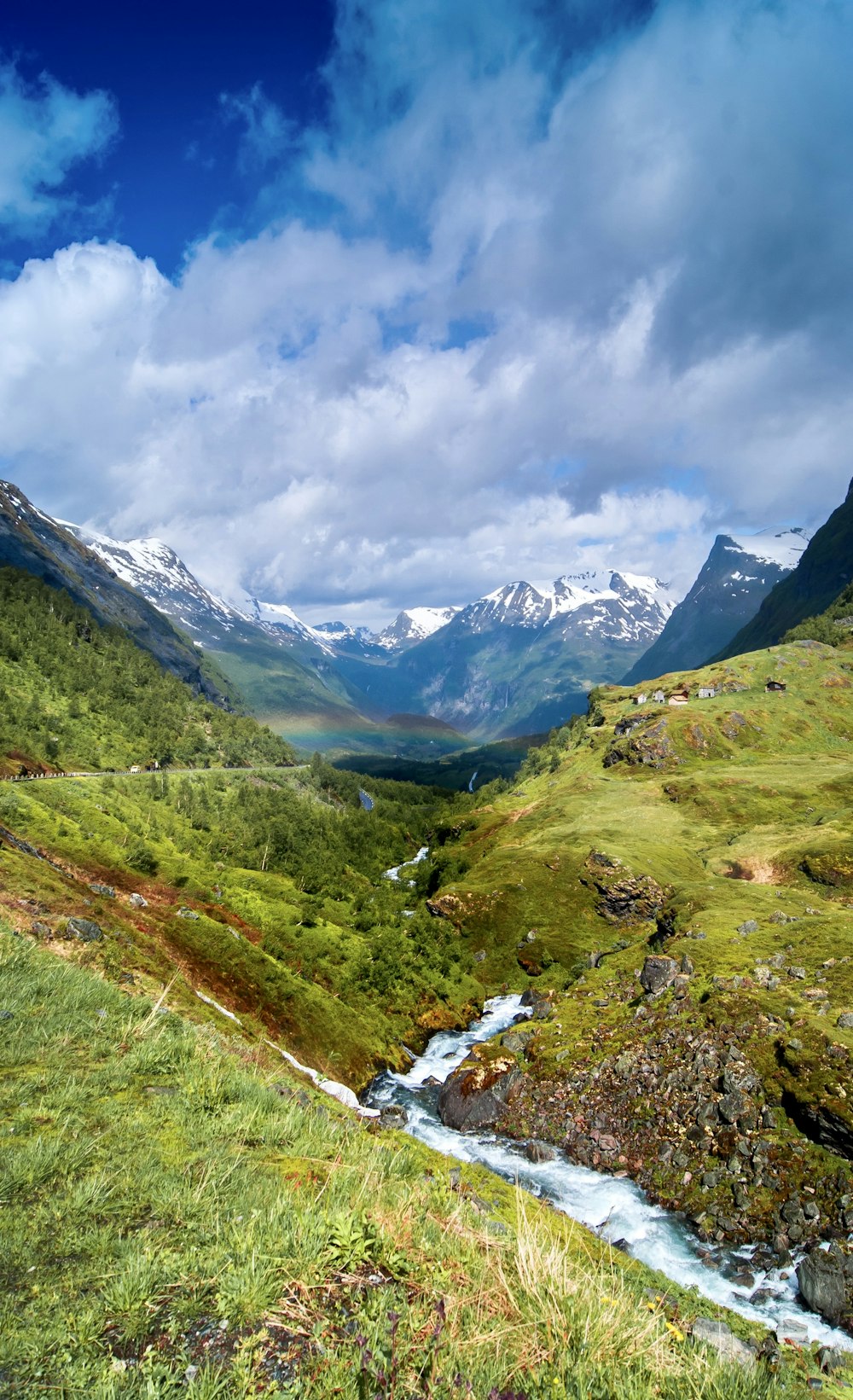 green grass field and mountains under white clouds and blue sky during daytime