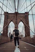 man in black jacket and black pants standing on brown bridge