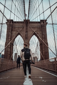 man in black jacket and black pants standing on brown bridge