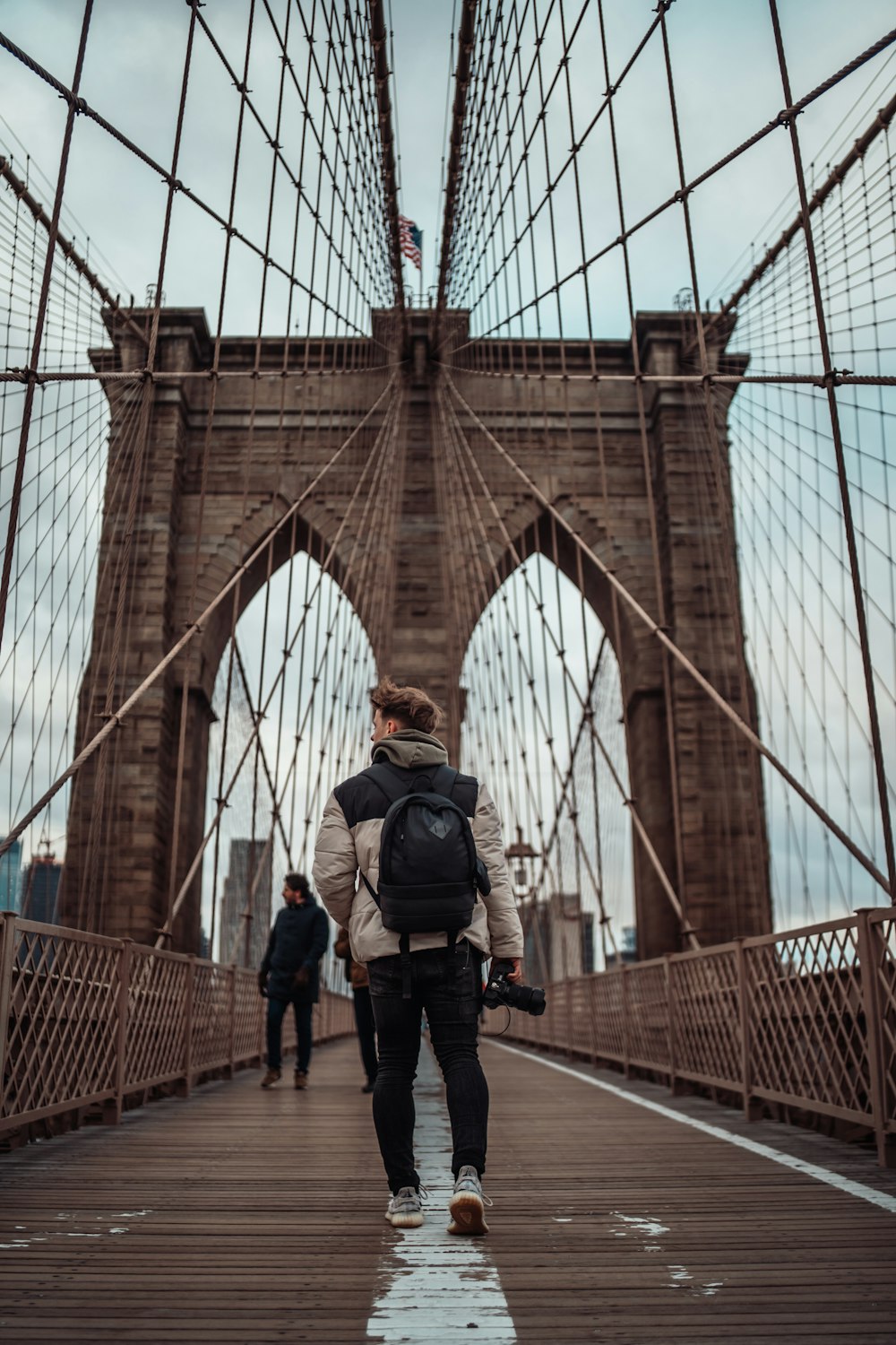 man in black jacket and black pants standing on brown bridge