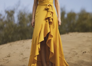 woman in yellow tube dress standing on brown sand during daytime