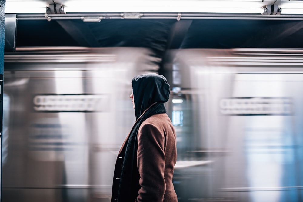 man in brown hoodie standing in front of train
