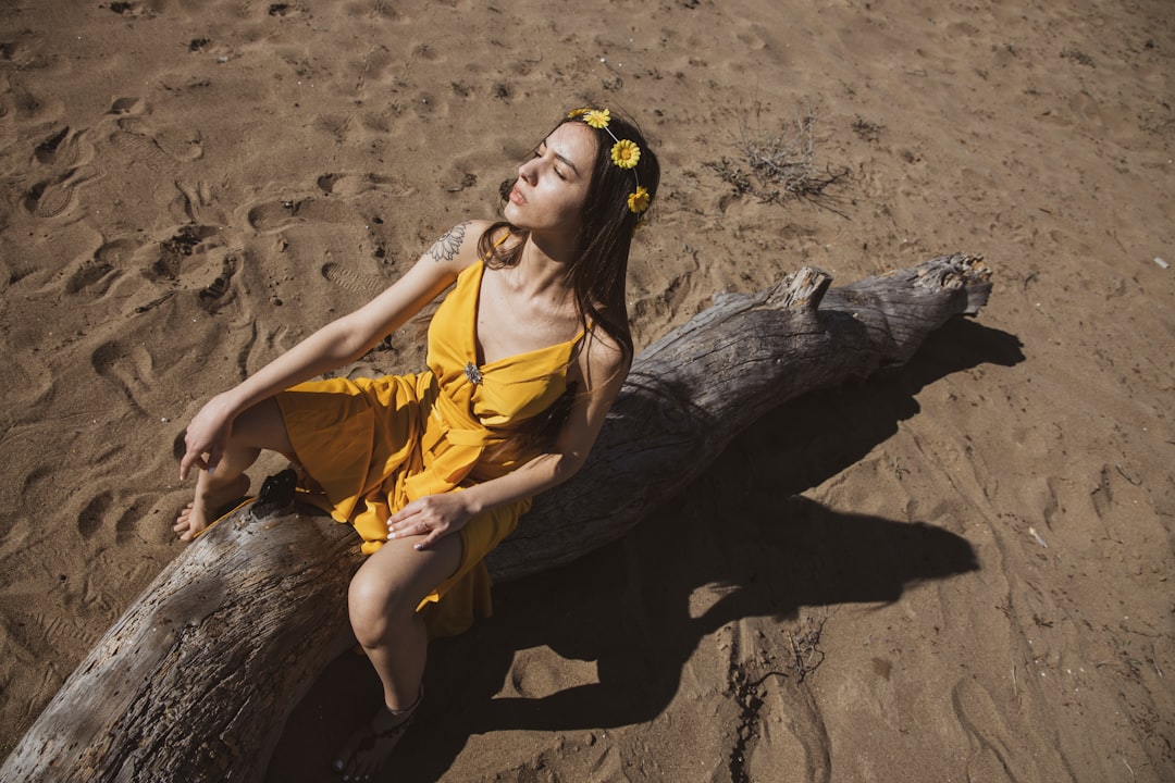 woman in yellow sleeveless dress sitting on brown tree trunk