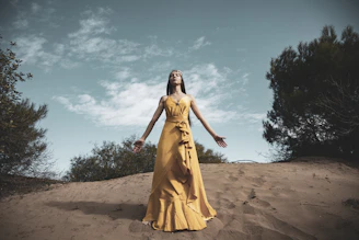 woman in yellow dress standing on brown sand under blue sky during daytime