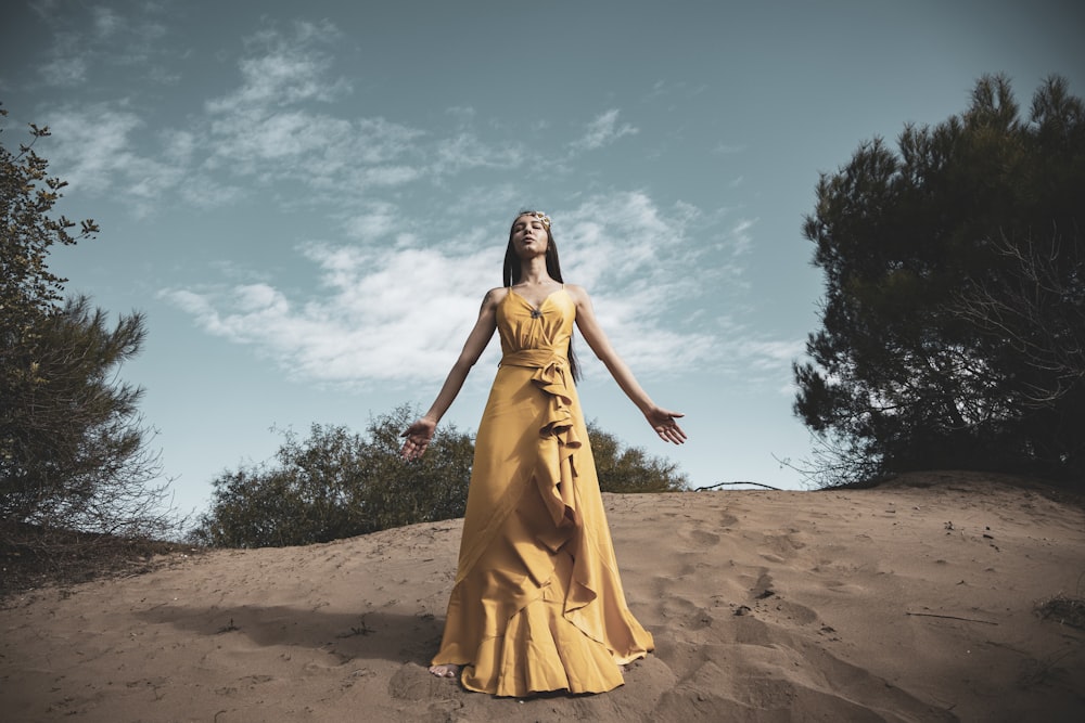 昼間、青空の下、茶色の砂浜に立つ黄色いドレスを着た女性