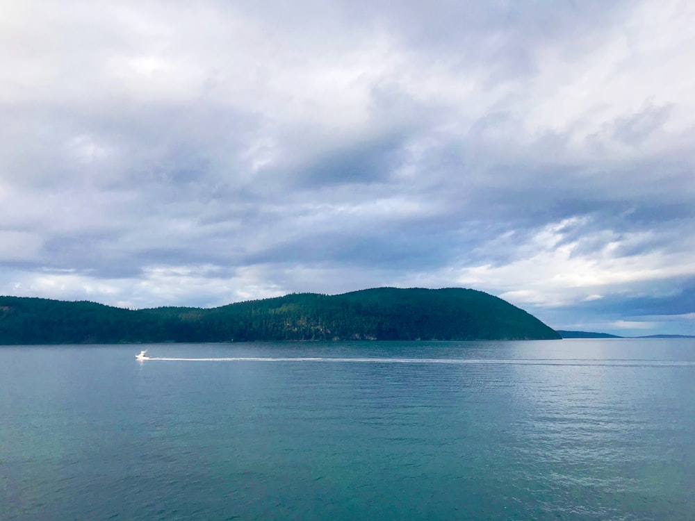 body of water near mountain under cloudy sky during daytime