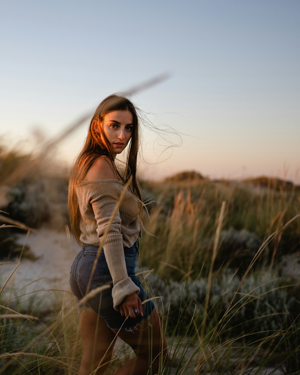 woman in brown long sleeve shirt and blue denim jeans standing on green grass field during