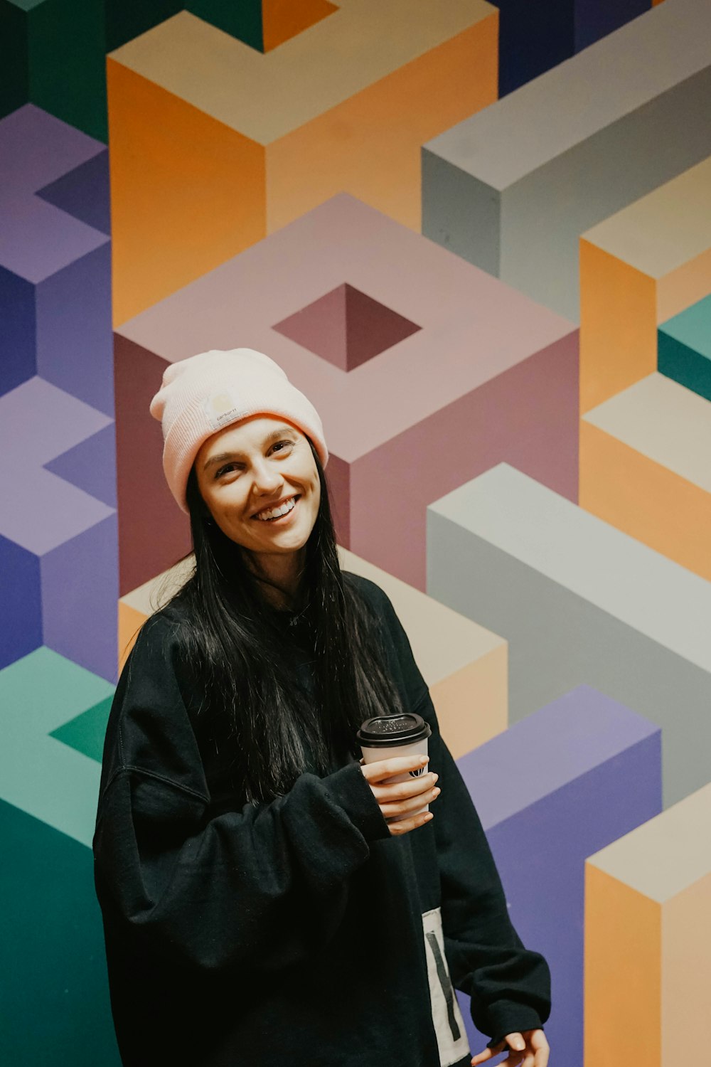 smiling woman in black coat holding black ceramic mug