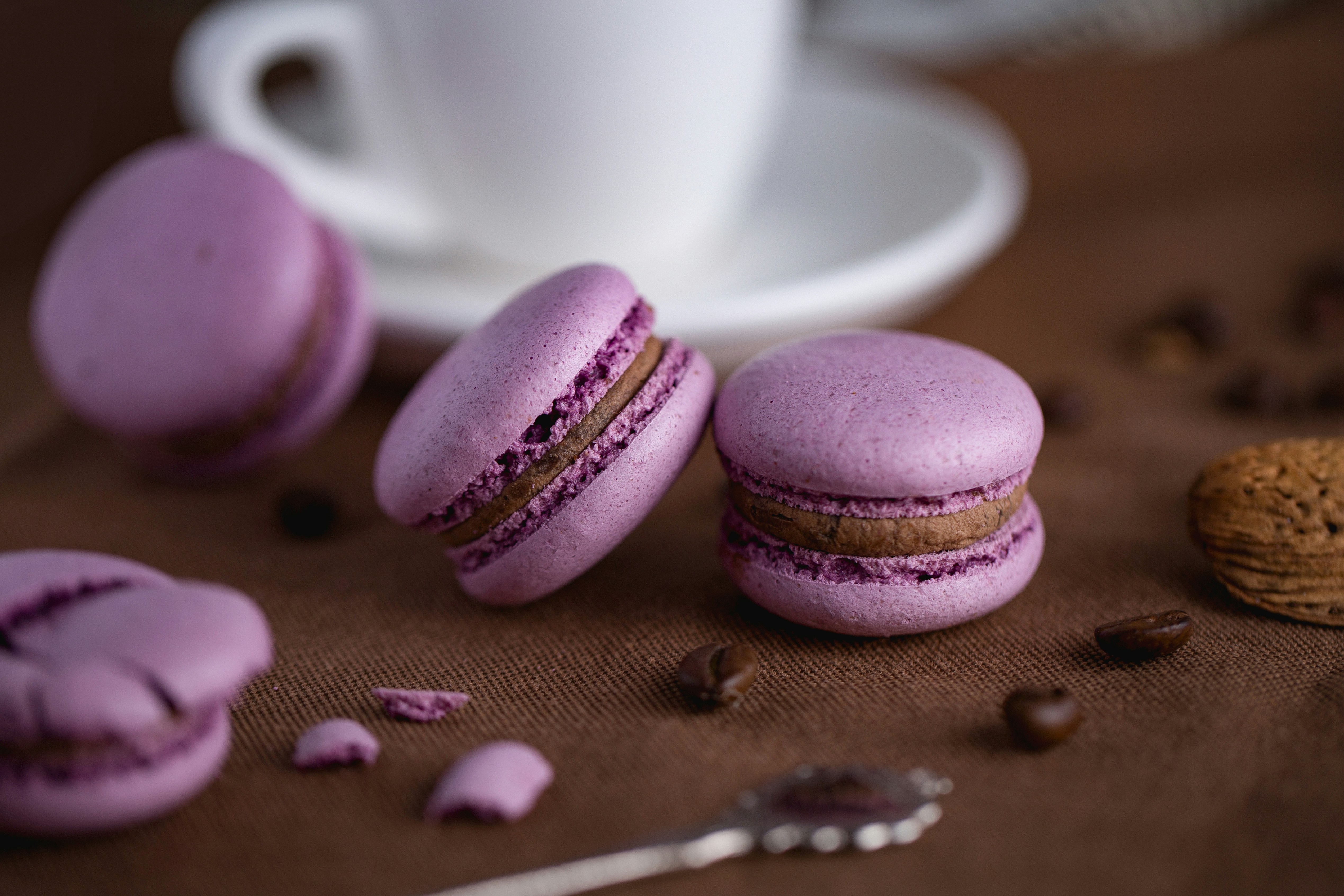 Des macarons violets fourrés au café, posés sur une nappe marron et entourés de grains de café.