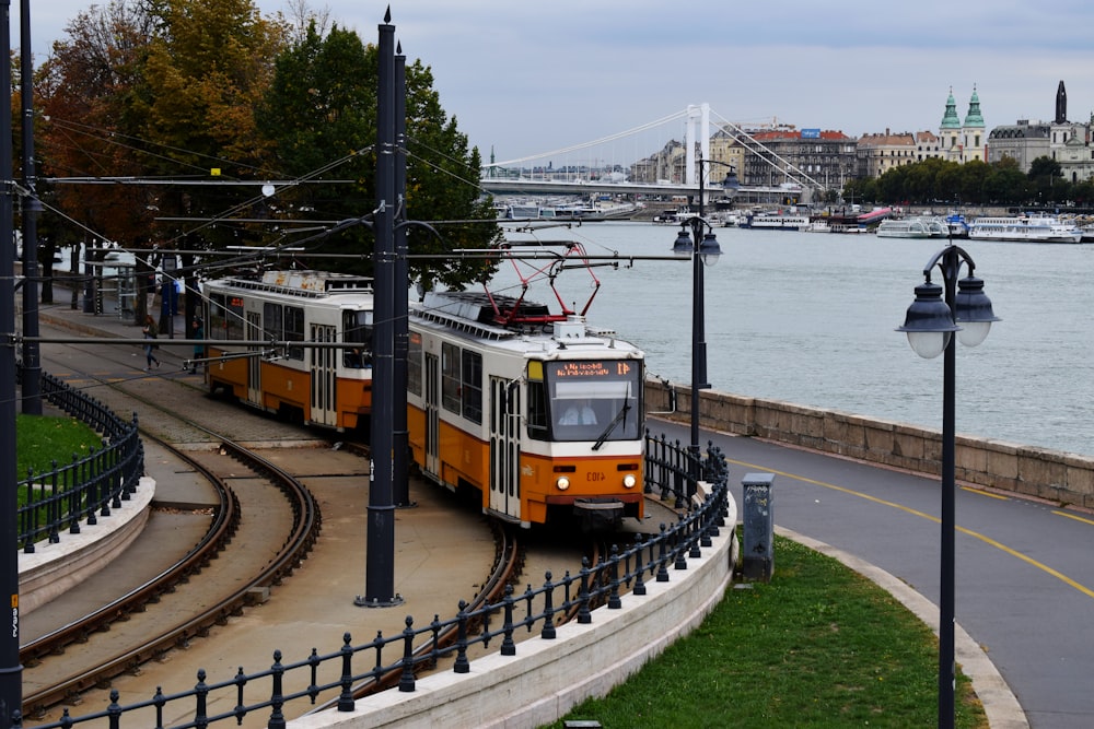 yellow and red tram on rail road near body of water during daytime