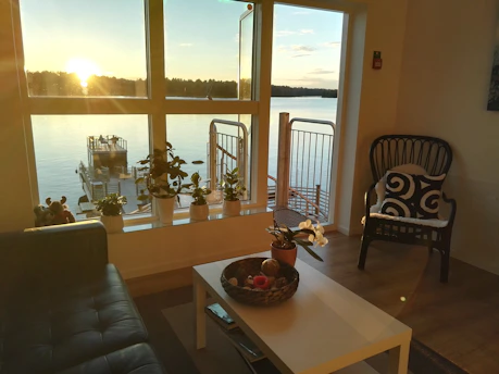 A serene living room featuring matte black accents, warm wood beams, and soft cream walls overlooking a lake view.