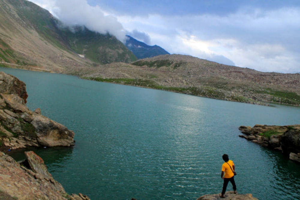 man in black shirt standing on rock near lake during daytime