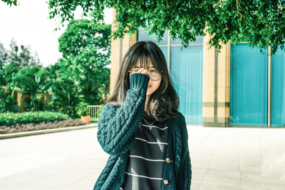 woman in gray coat standing near green tree during daytime