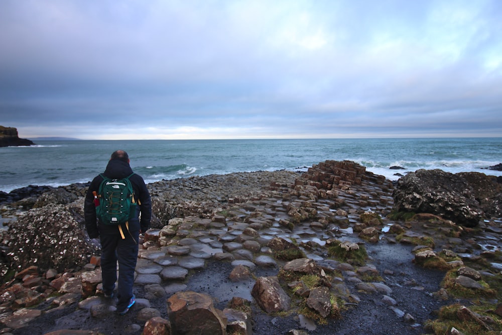 검은 재킷을 입은 남자가 낮에 바위 해안에 서 있습니다.